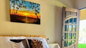 A hotel room with a bed, pillows, a painting, and a door. - The Jungle Guriú (Camocim)