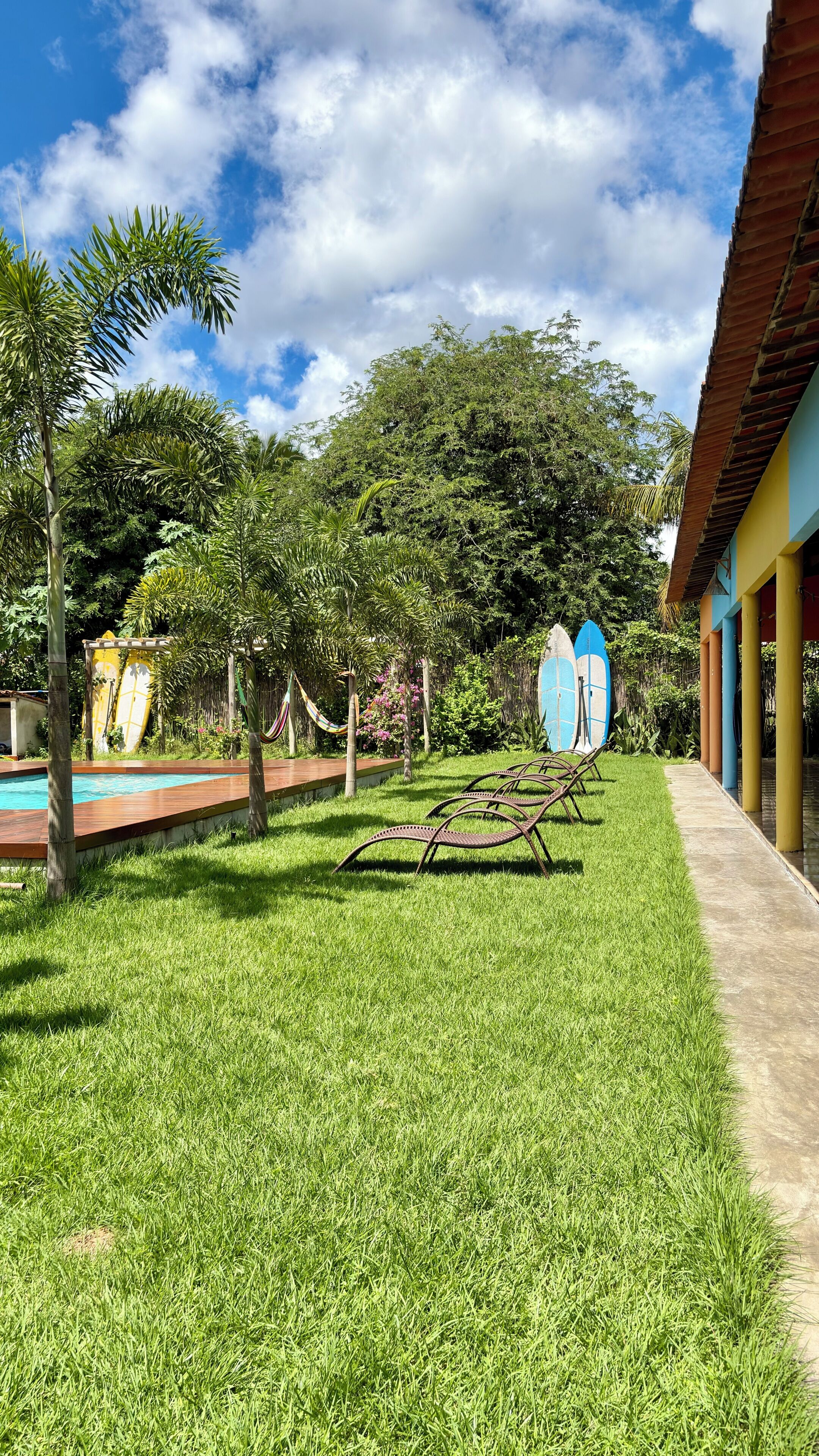 Un espace piscine avec pelouse, un hamac et des planches de surf.