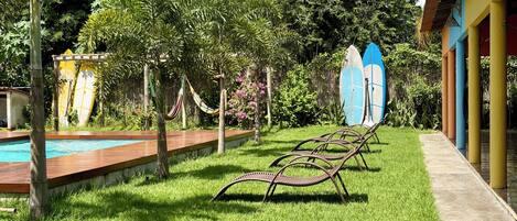 Un espace piscine avec pelouse, un hamac et des planches de surf.
