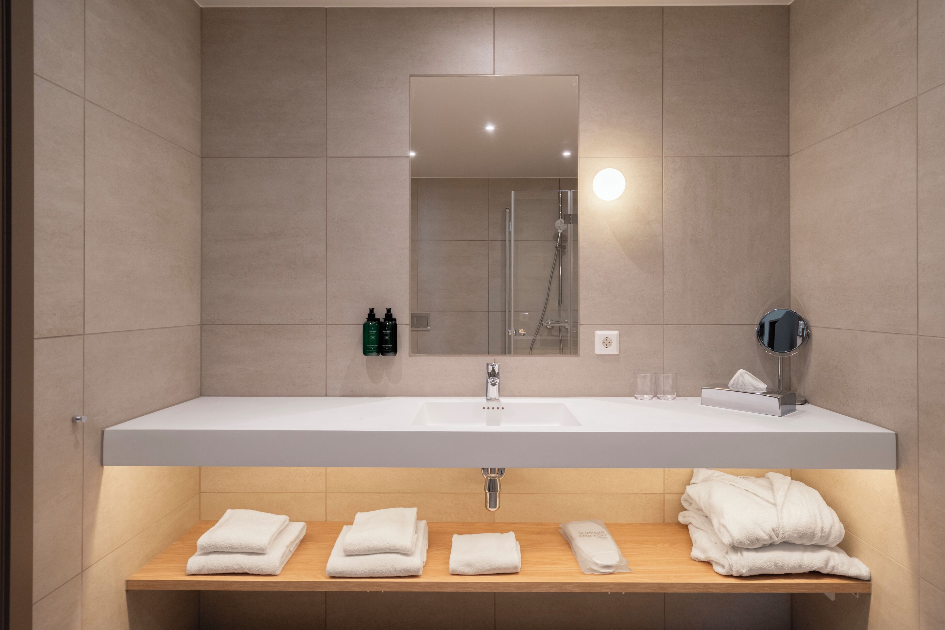 A modern bathroom with a large mirror, a shower, and a vanity with towels.