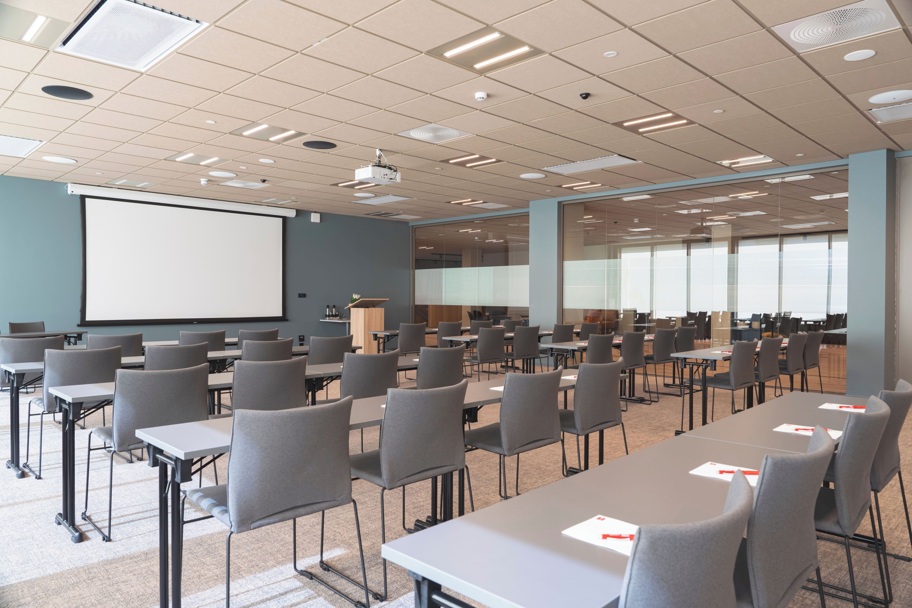 A conference room with rows of tables and chairs, a projector screen, and a large window.