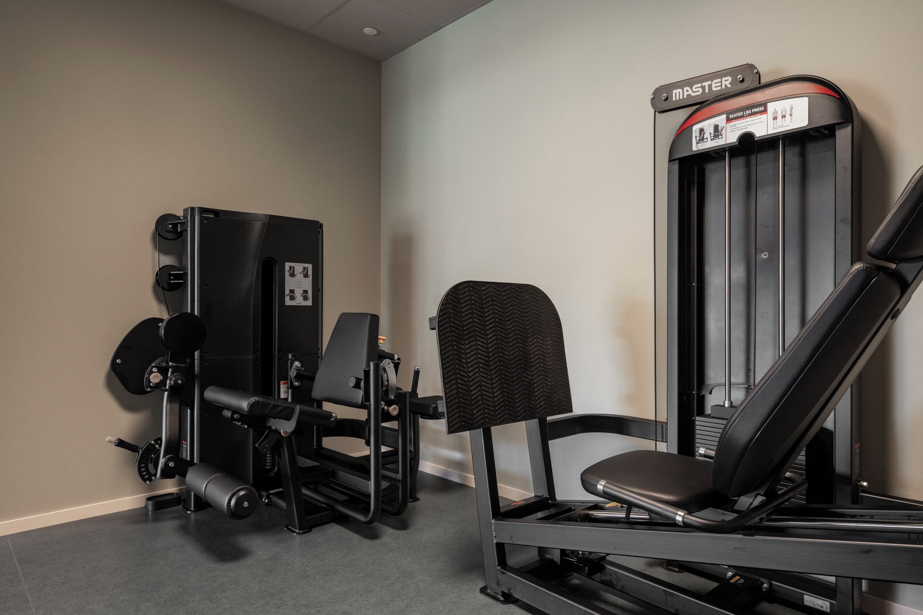 Ett gym med en sittande benpressmaskin, en viktmagasin och en bänk.