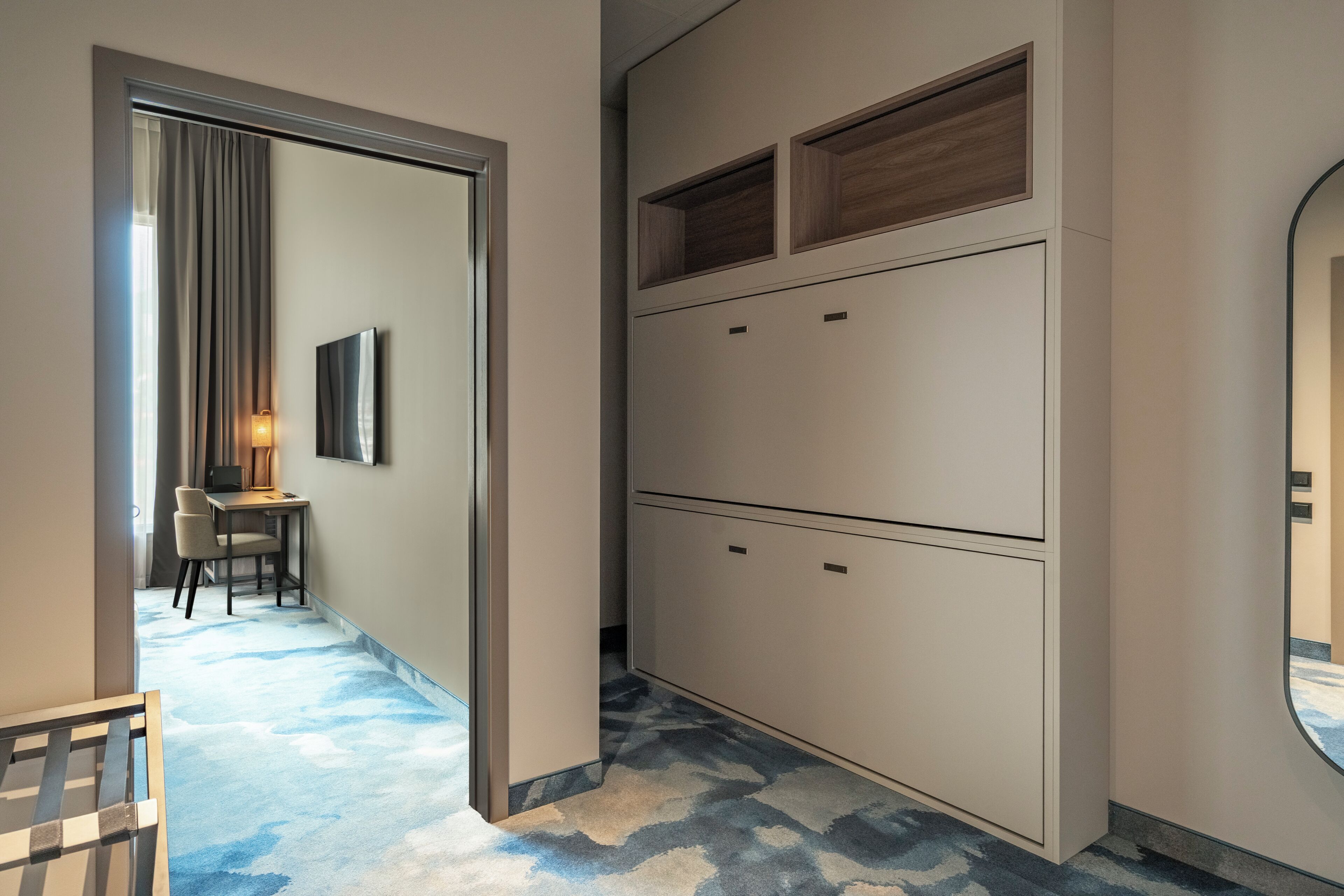 A hotel room with a desk, chair, and a large wardrobe with multiple doors.