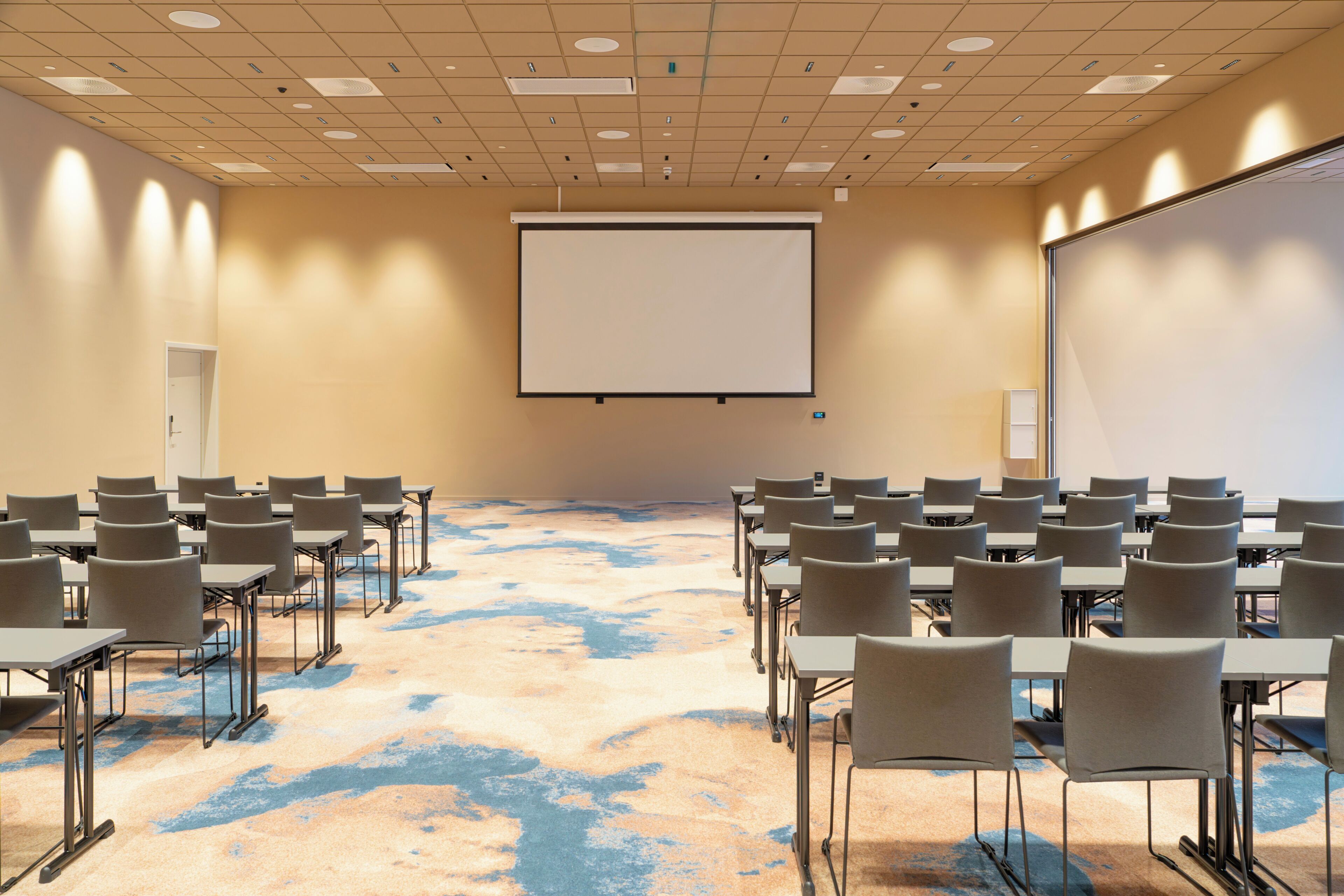 A conference room with a large projection screen, multiple tables, and chairs arranged for meetings.