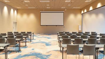 A conference room with a large projection screen, multiple tables, and chairs arranged for meetings.