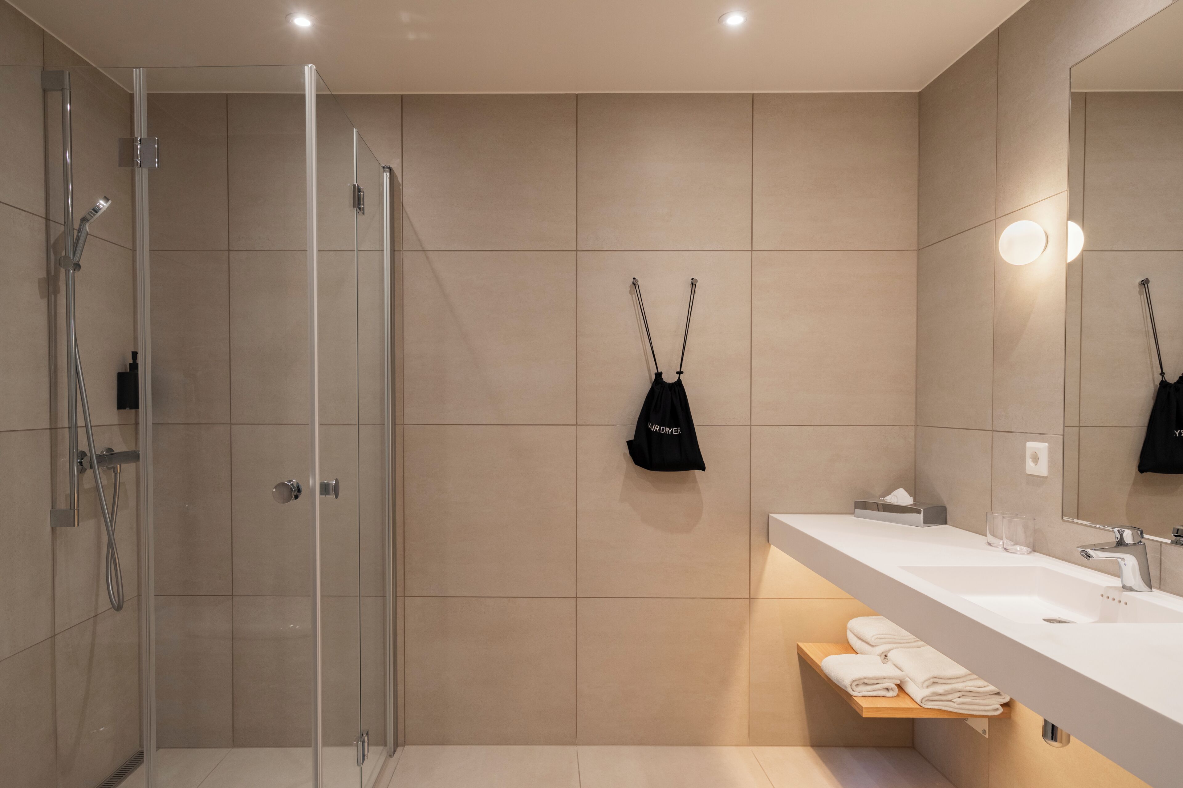 Ein modernes Badezimmer mit Duschkabine aus Glas, einem weißen Waschbecken mit Handtuchhalter und einem Spiegel.