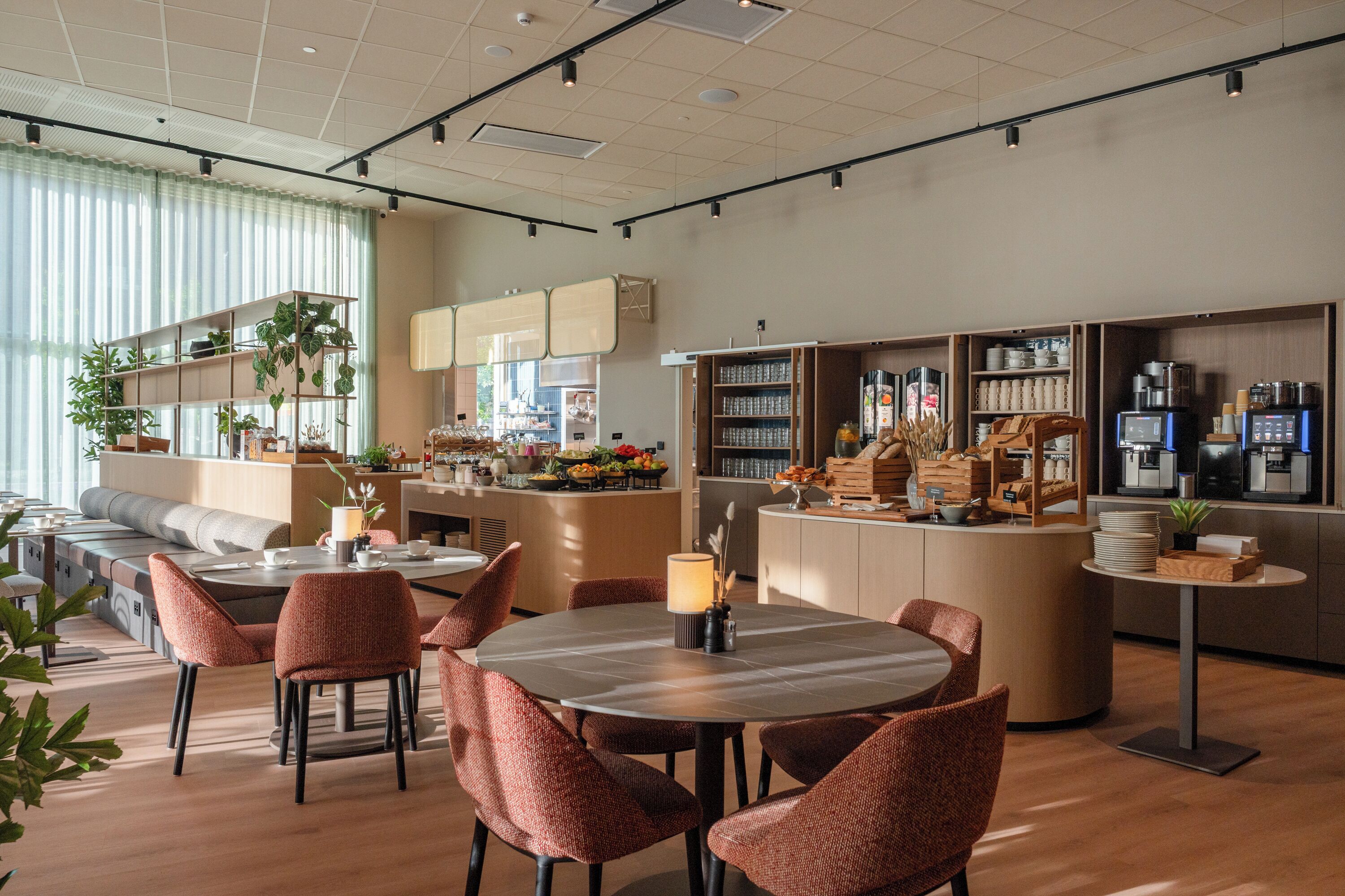 A modern cafe interior with seating arrangements, a counter with coffee machines, and shelves stocked with various items.