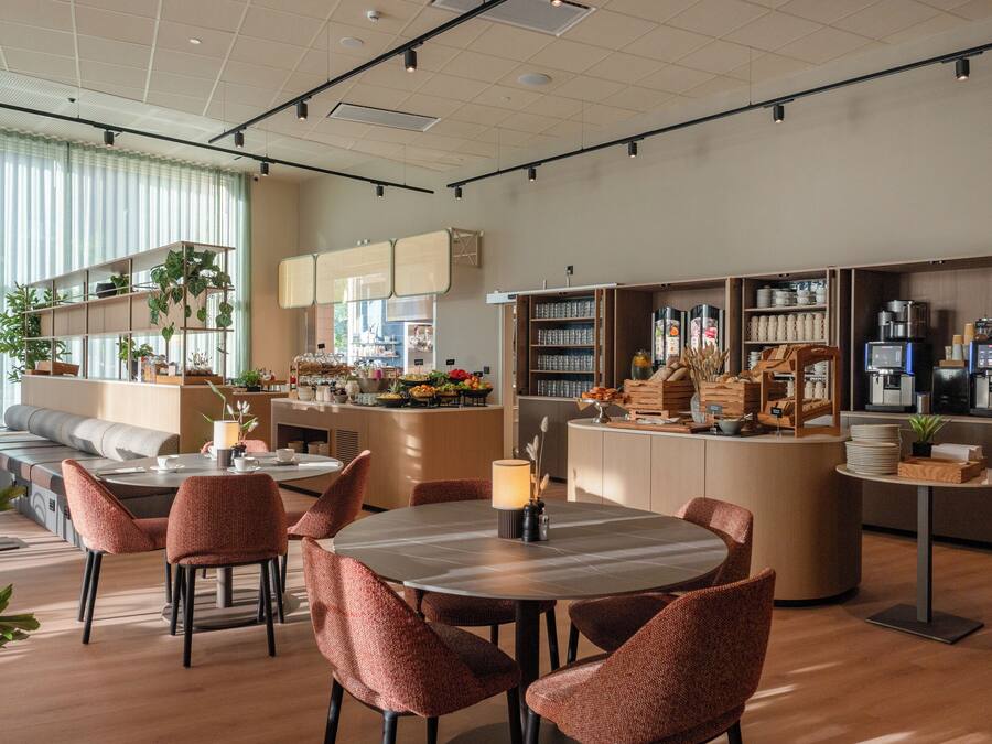 A modern cafe interior with seating arrangements, a counter with coffee machines, and shelves stocked with various items.