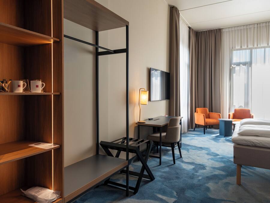 Una habitación de hotel con escritorio, dos sillas, cama, televisor y armario.