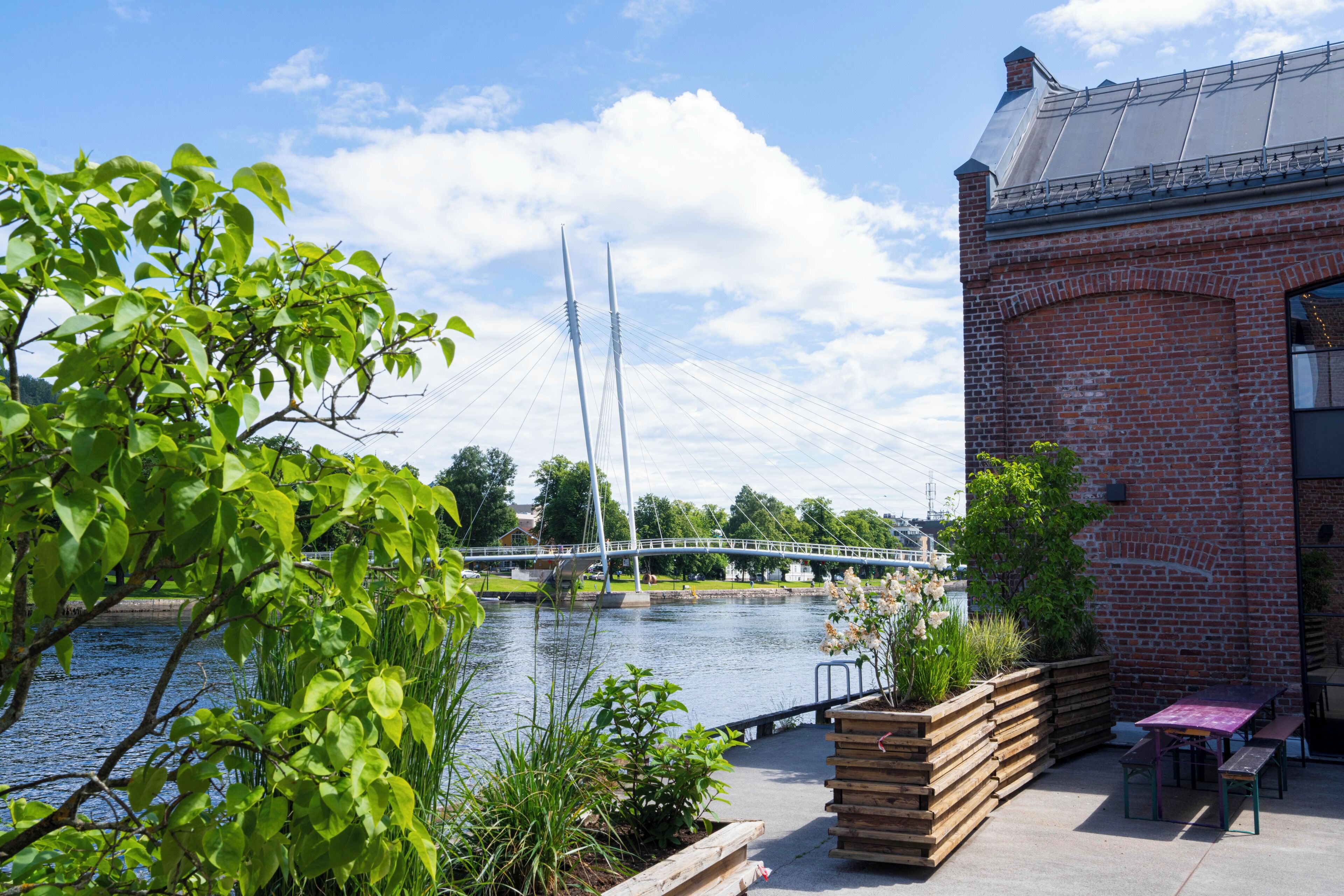 A riverside view with a bridge, a brick building, and a wooden bench area.
