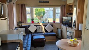 A compact living space with a sofa, ottoman, and a small table with bottles.