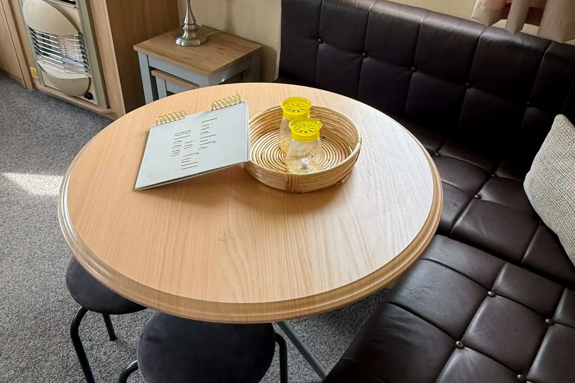 A round wooden table with a spiral notebook and a woven basket containing yellow objects.