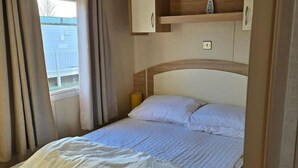 A single bed with white bedding, a wooden headboard, a bedside lamp, and a window with curtains.