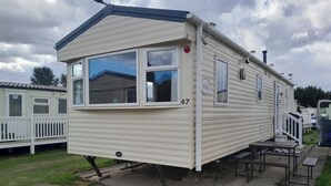 A mobile home with a balcony, a patio table, and a small deck.