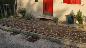 A two-story building with red shutters, a stone-paved entrance, and a small garden area. - Casa Florian (Vito d'Asio)