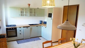 A kitchen with light green cabinets, a stove, a microwave, and a dining area with a table and chairs. - Casa Florian (Vito d'Asio)