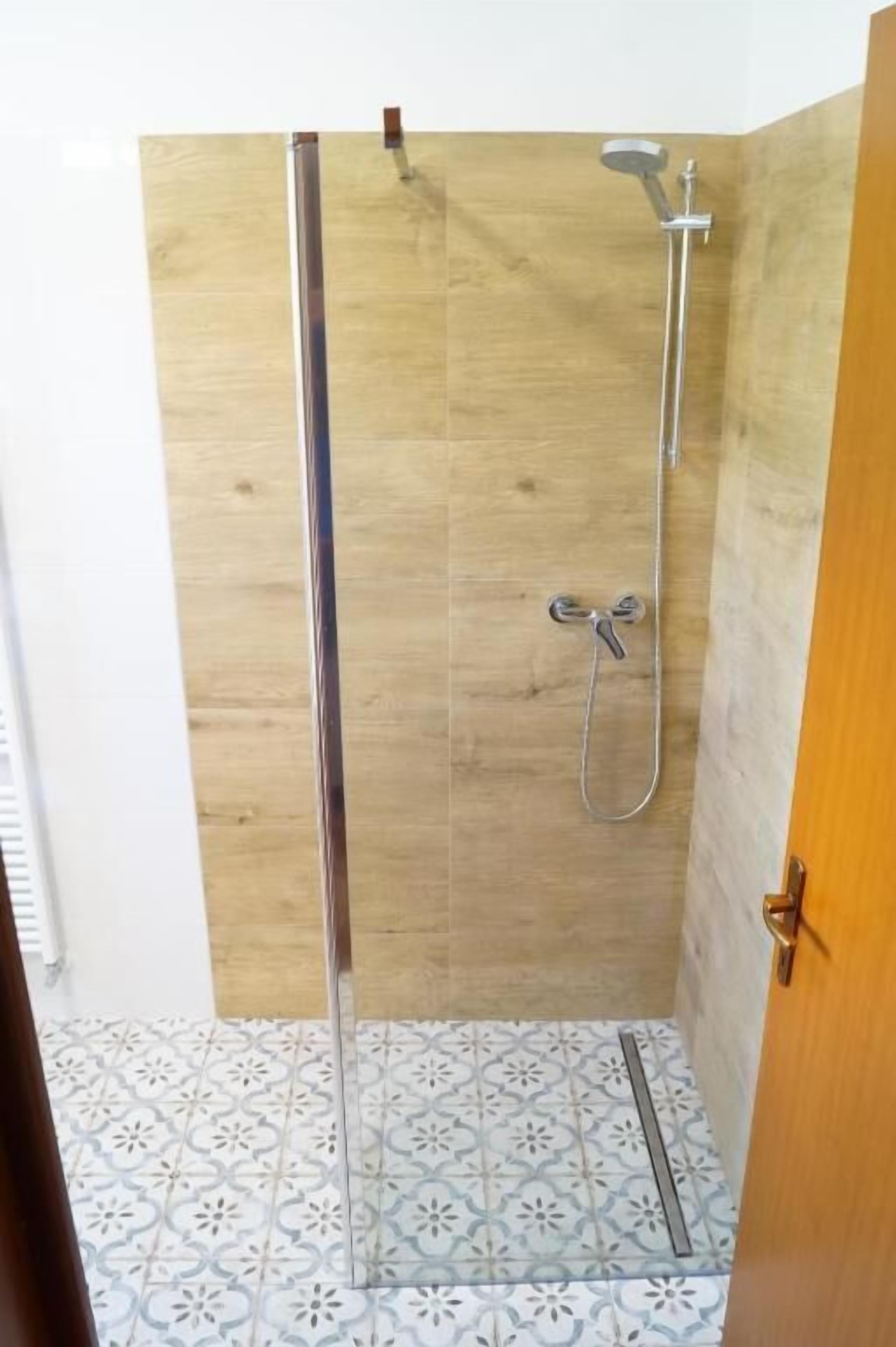 A shower with a wooden wall and a tiled floor.