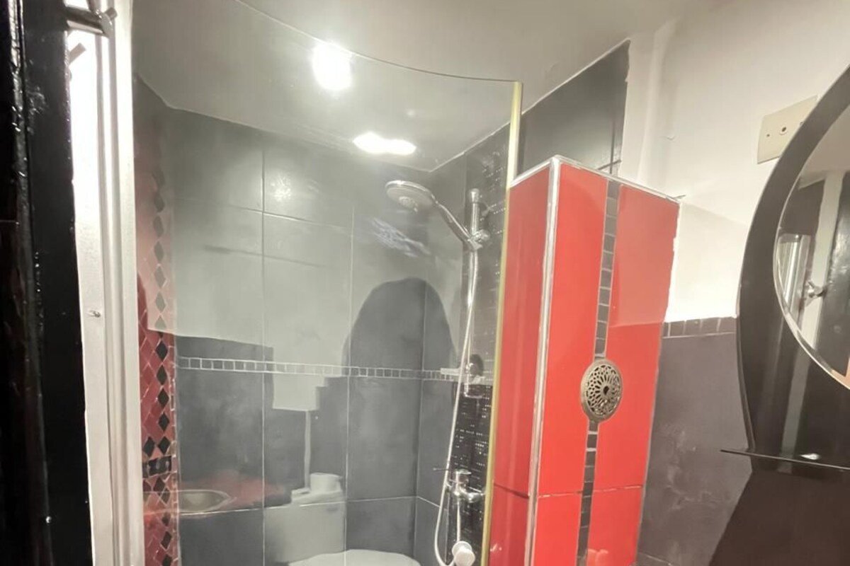 A bathroom with a glass-enclosed shower, a red vanity, and a mirror.