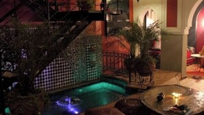 An indoor pool area with a spiral staircase, seating, and a small table with a candle. - Riad Kantarell (Marrakech)