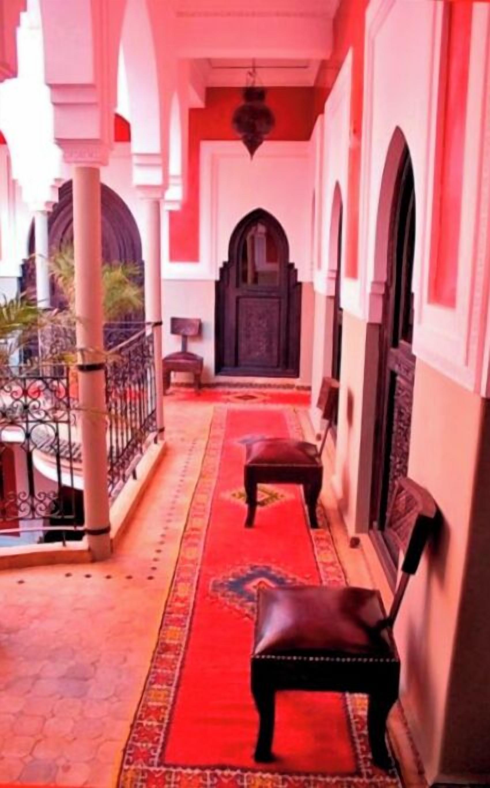 A covered outdoor area with a red carpet, a bench, and a dark door.