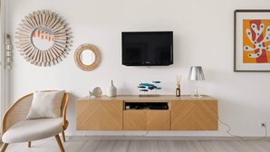 Una sala de estar moderna con un mueble de madera, un televisor, una silla de mimbre, objetos decorativos y una obra de arte enmarcada.