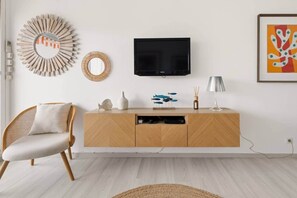A modern living room with a wooden cabinet, a television, a wicker chair, decorative items, and a framed artwork. - Studio city center free parking (Saint-Tropez)
