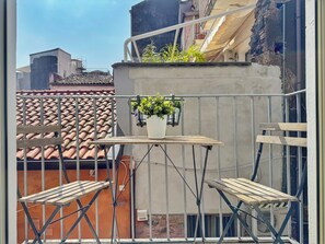 A balcony with a small table and two wooden chairs, a potted plant, and a metal railing. - [5 Min from the Duomo] Quiet & Central Apartment • Historic Center of Catania (Catania)