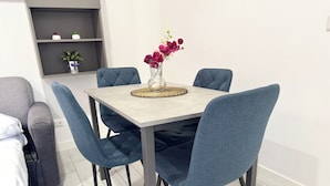 Ein Essbereich mit Tisch, Stühlen, einer Vase mit Blumen und einem Regal mit Pflanzen.