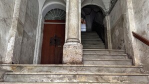 Eine imposante Treppe mit Marmorstufen und klassischen Säulen, die zu einer Holztür oben hinaufführt.