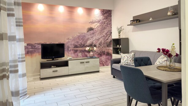 Ein modernes Wohnzimmer mit Flachbildfernseher, einer Couch, einem Esstisch mit Stühlen und einer dekorativen Wandmalerei.