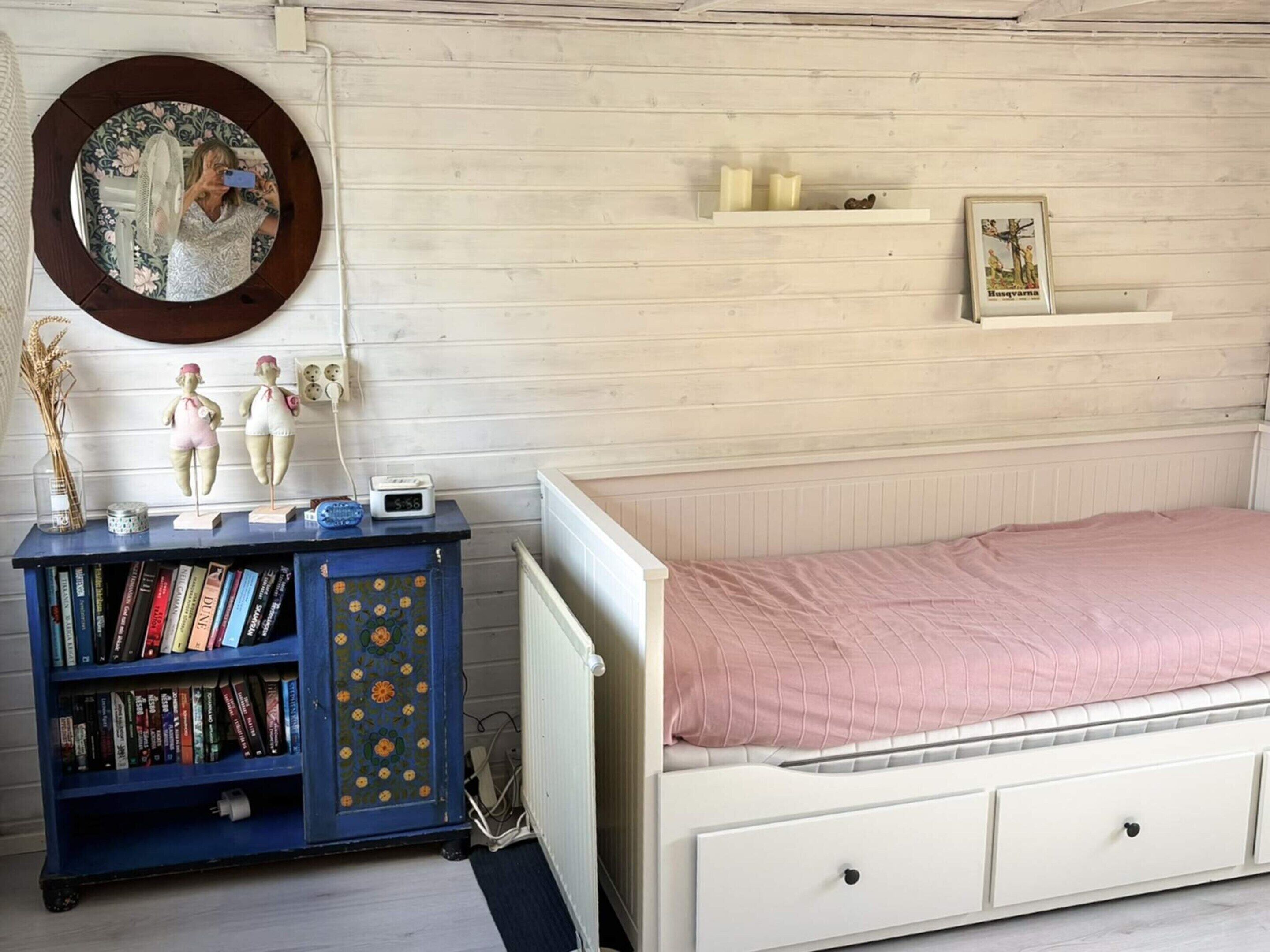 A bedroom with a white bed, a blue bookshelf, a mirror, and a wall clock.