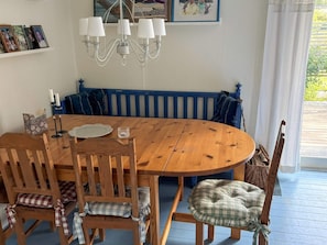 A dining area with a wooden table, chairs, a bench, a chandelier, and framed pictures on the wall.