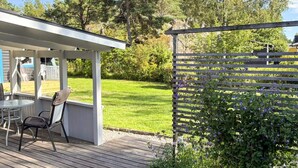 A covered outdoor seating area with a table and chairs, a wooden deck, and a garden with a wooden fence and flowering plants. - 4 Star Holiday Home in Sorunda (Sorunda)