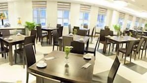 Moderni ravintola, jossa on useita pöytiä ja tuoleja, tiskialue sekä suuret ikkunat, joista pääsee sisään runsaasti luonnonvaloa.