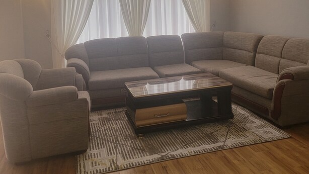 Een moderne woonkamer met een hoekbank, een bijzettafeltje en een kamerbreed tapijt.
