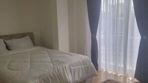 Een slaapkamer met een bed, een raam met gordijnen en een vloerkleed.
