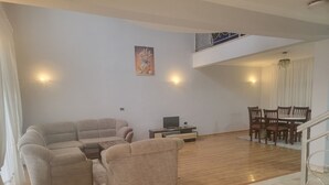 Een woonkamer met een hoekbank, een televisie, een eettafel met stoelen en een trap.