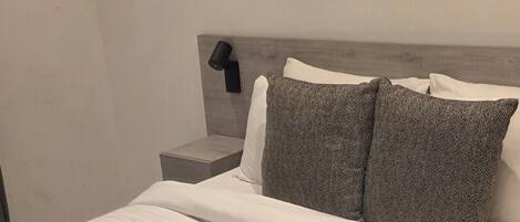 A neatly made bed with a rolled towel, a headboard, and two pillows.