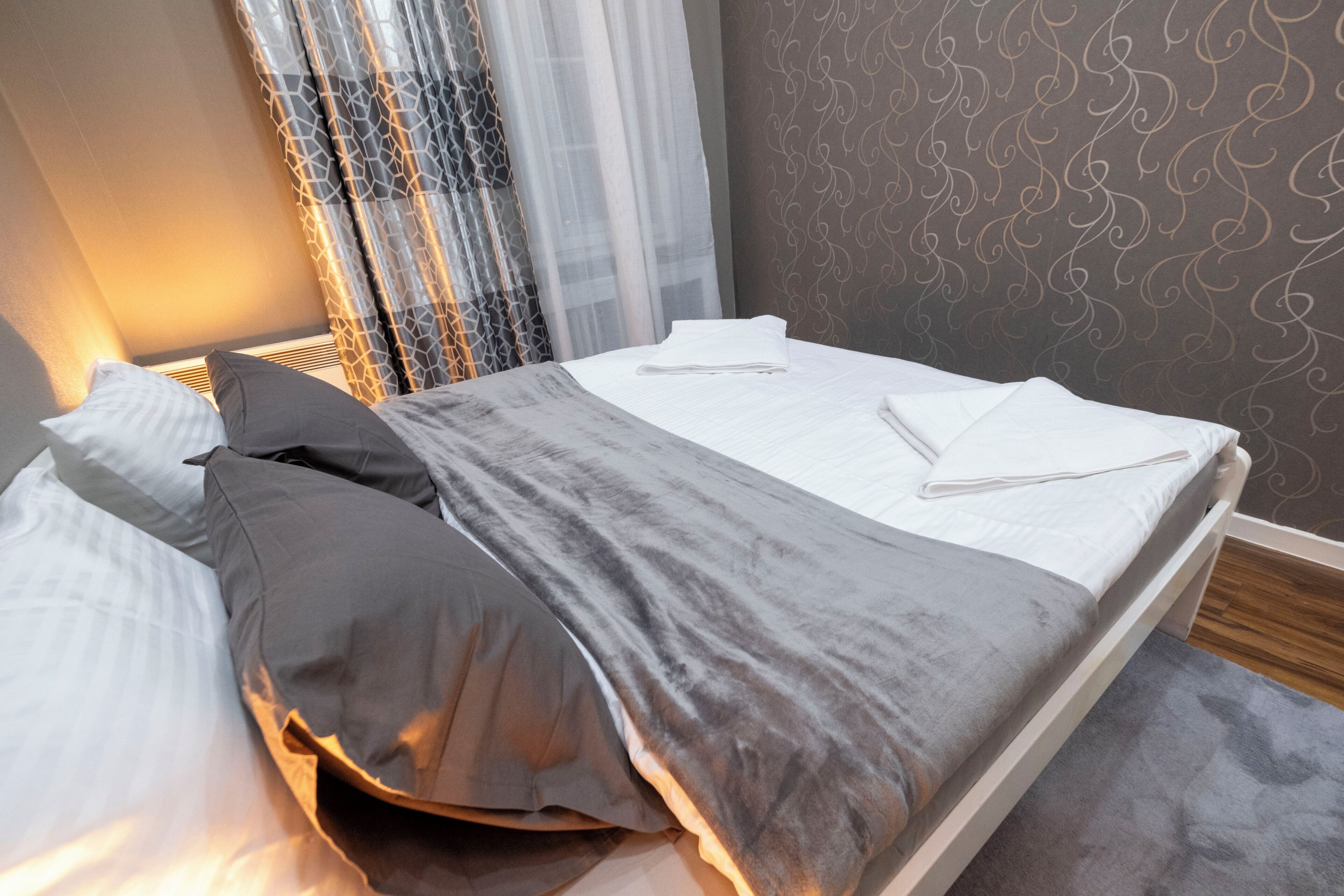 A neatly made bed with pillows, a bedside table, and a wall with a patterned wallpaper.