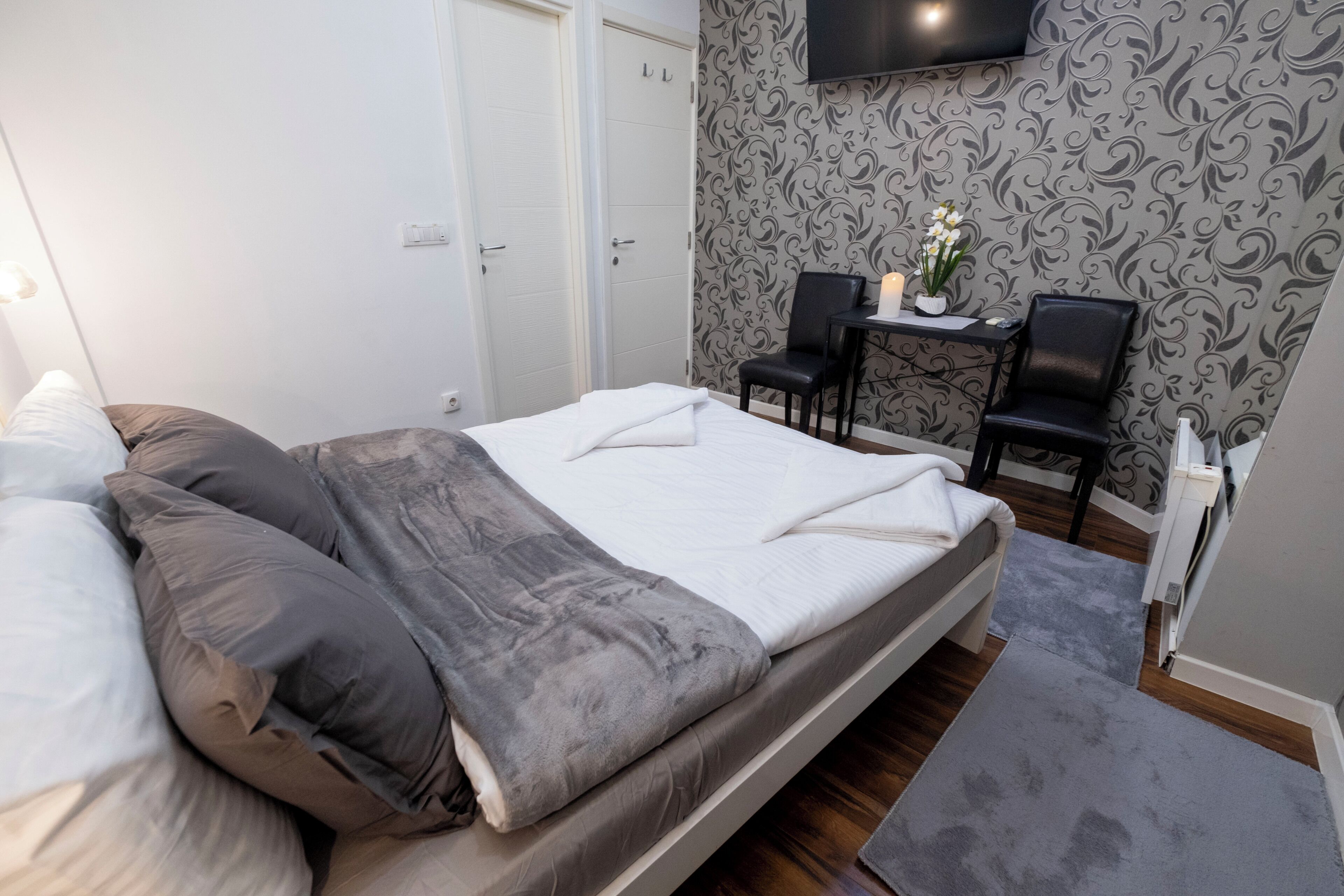 Ein Schlafzimmer mit einem Bett, einem Schreibtisch, zwei Stühlen, einem Fernseher und einer Wand mit Muster.
