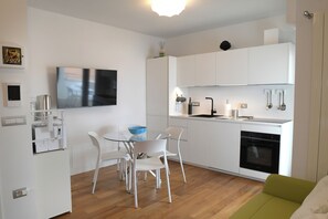 Een moderne keuken met witte kastjes, een ingebouwde oven en een eethoek met een glazen tafel en witte stoelen.