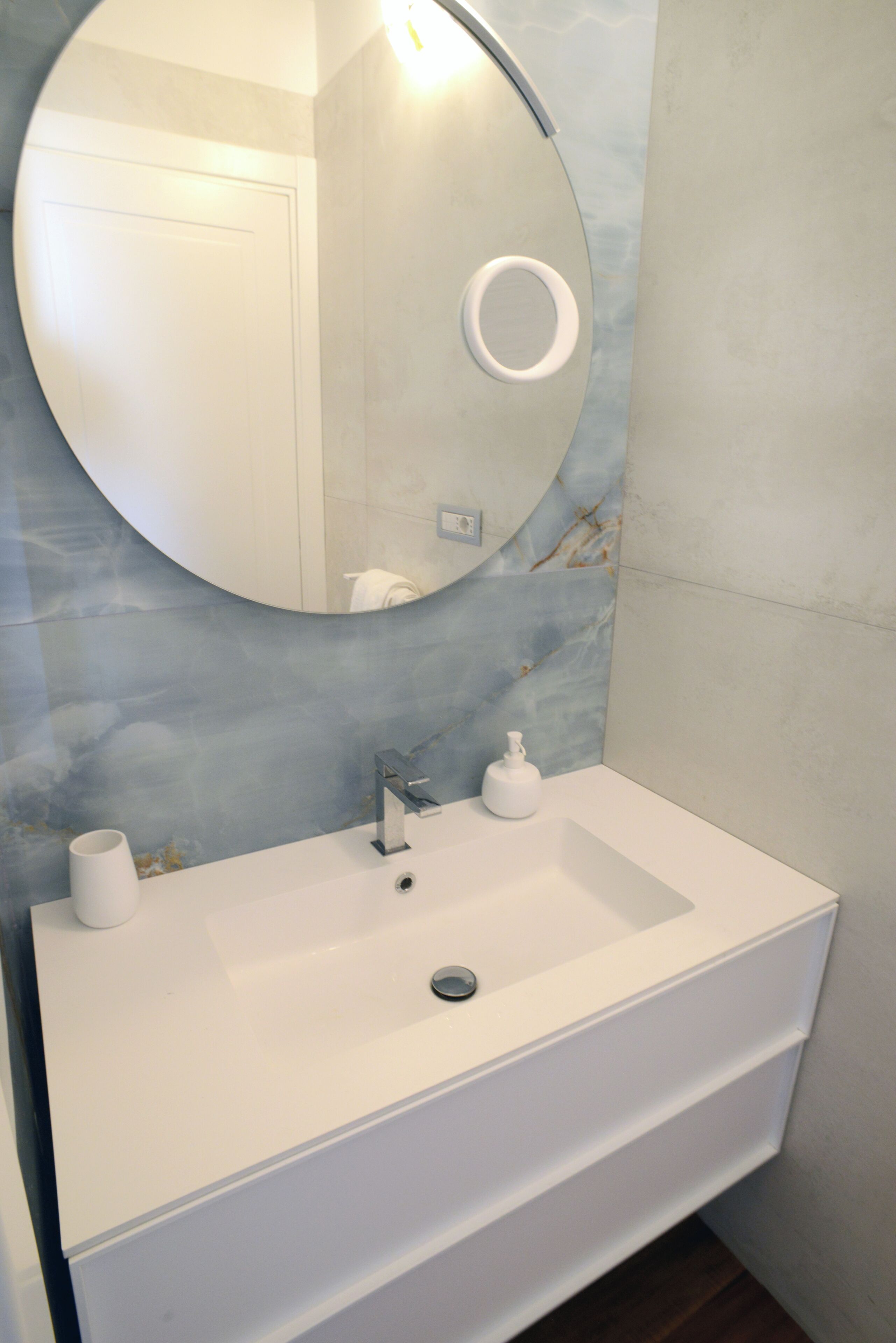 A bathroom with a white sink, a round mirror, and a marble-patterned wall.