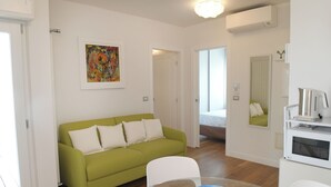 A modern living room with a green sofa, a dining table with a blue bowl, and a kitchen area with an oven. - Lecasinedigiò2 Cozy and refined apartment with sea view terrace (Alghero)