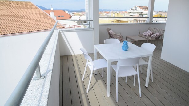 A balcony with a white table and chairs, a blue vase, and a view of buildings. - Lecasinedigiò2 Cozy and refined apartment with sea view terrace (Alghero)