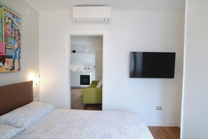 Een slaapkamer met een bed, een aan de muur bevestigde televisie en een deur naar een woongedeelte.