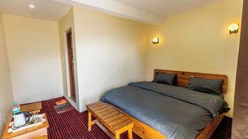 A bedroom with a bed, a wooden bench, a small table with a kettle, glasses, and a water bottle.