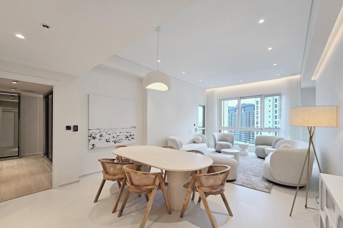 A modern living room with a large white sofa, a dining table with chairs, and a floor lamp.