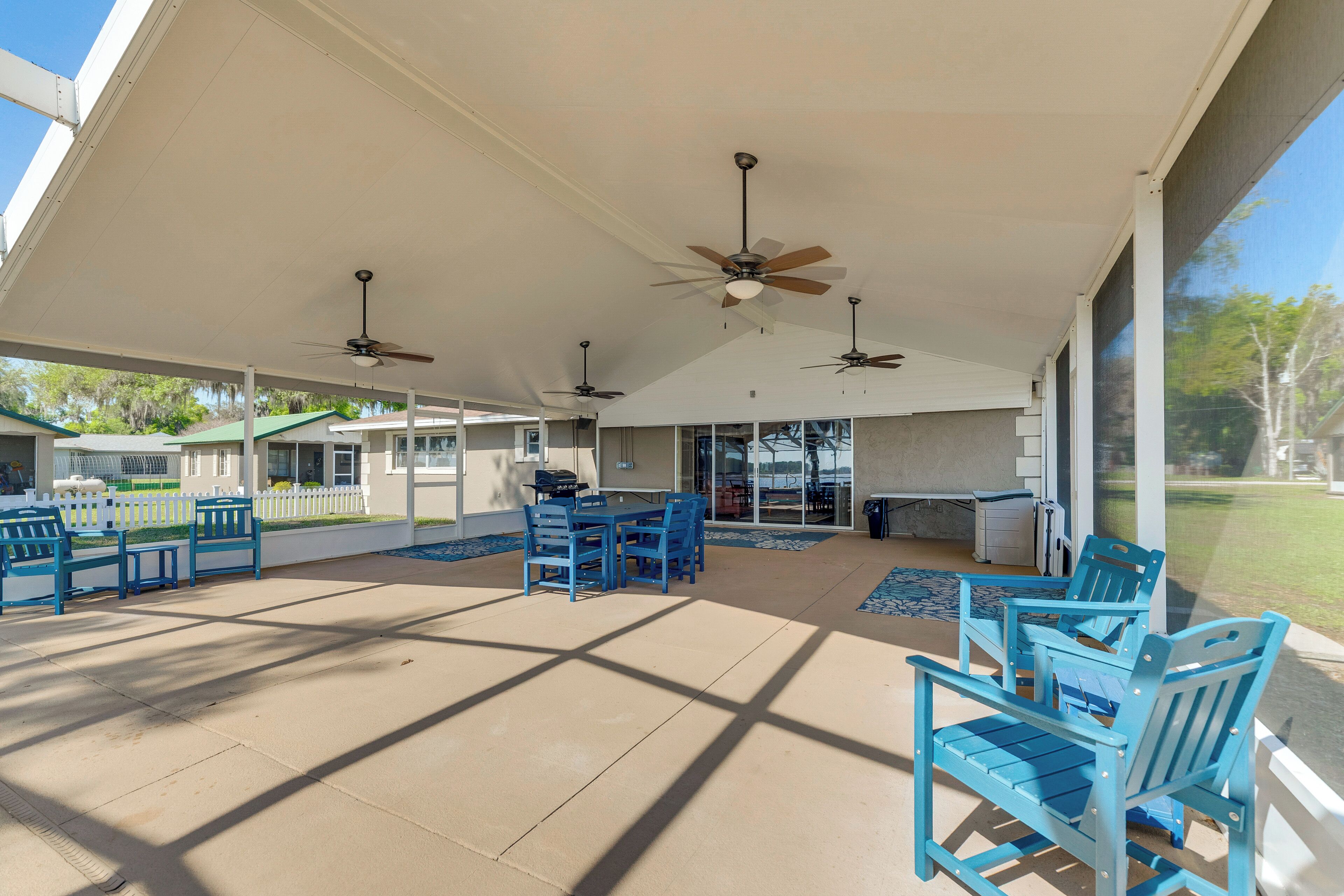 Un patio techado al aire libre con sillas y mesas azules, ventiladores de techo y vistas del entorno.