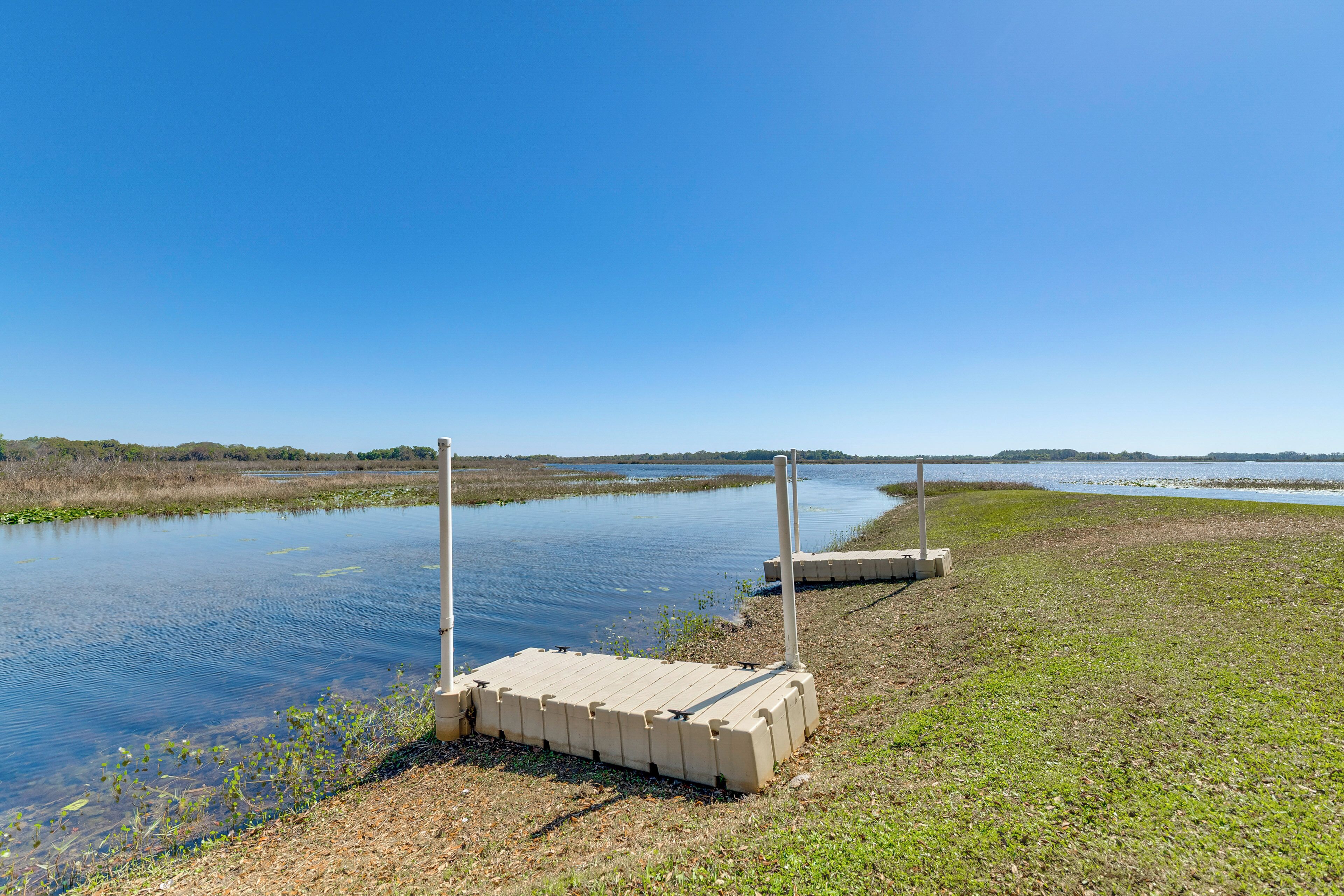 A calm water body with a concrete dock extending into it, surrounded by grassy areas and distant trees.