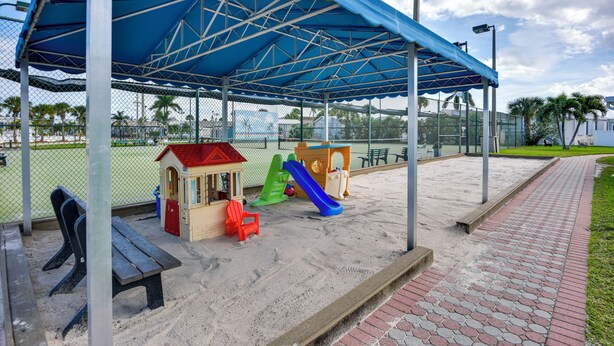 A covered play area with a sandpit, benches, and a small building with a slide. - Waterfront Resort Home! Extended Jensen Beach Stay (Jensen Beach)